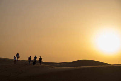 People in desert against sky during sunset