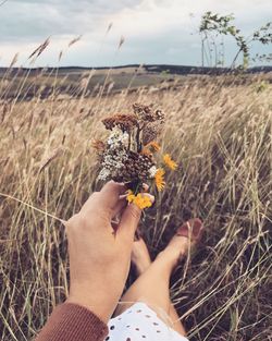 Low section of woman holding flower while sitting on land