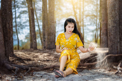 Smiling woman throwing sand while sitting on tree trunk