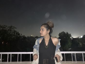 Portrait of beautiful young woman standing by railing against sky