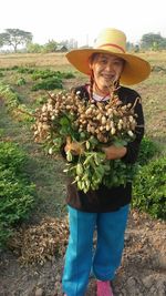 Portrait of smiling woman holding vegetables while standing in farm