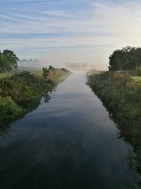 River amidst field against cloudy sky