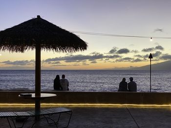 Silhouette people sitting by sea against sky during sunset