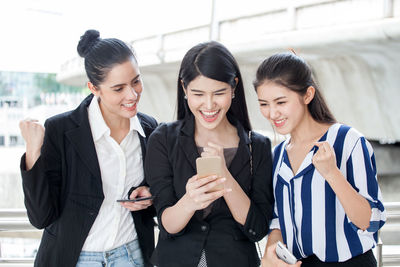 Young woman using phone while standing on laptop