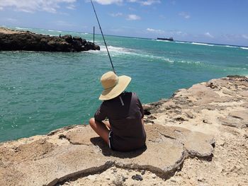 Rear view of woman sitting on shore against sea