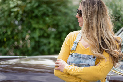 Woman with arms crossed standing by car