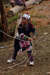 Happy girl in traditional clothing playing with rope on land