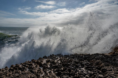 Waves splashing on rocks at shore against sky