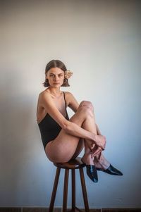 Portrait of young woman sitting on chair against wall