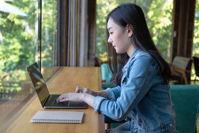 Side view of young woman using phone while sitting on table