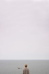 Rear view of woman looking at seagull flying over sea against clear sky