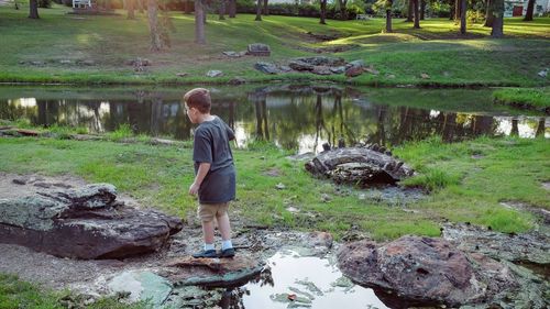 Full length of boy standing on rock by pond against trees in park