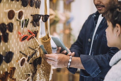 Man photographing label on sunglasses at rack by daughter in fashion store