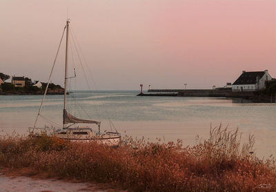 Sailboats moored in sea against clear sky during sunset