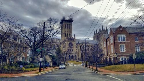 Street amidst buildings in city against storm clouds