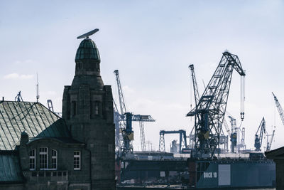 Cranes on pier amidst buildings in city against sky