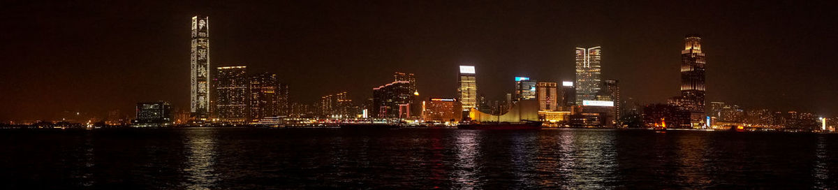 Illuminated buildings by river against sky at night