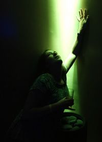 Sensuous woman with drink posing against illuminated wall