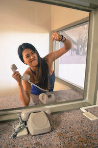 Woman holding telephone seen through glass