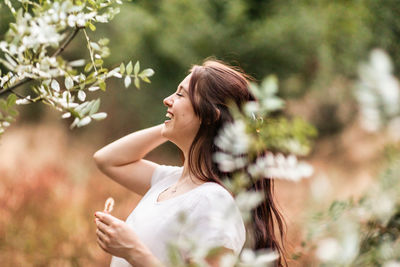 Side view of young woman standing against plants