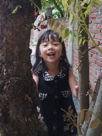 Close-up of smiling girl standing against tree trunk