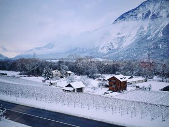 Snow covered houses by building against sky