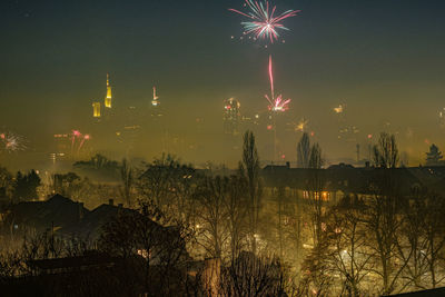 Firework display over illuminated city against sky at night