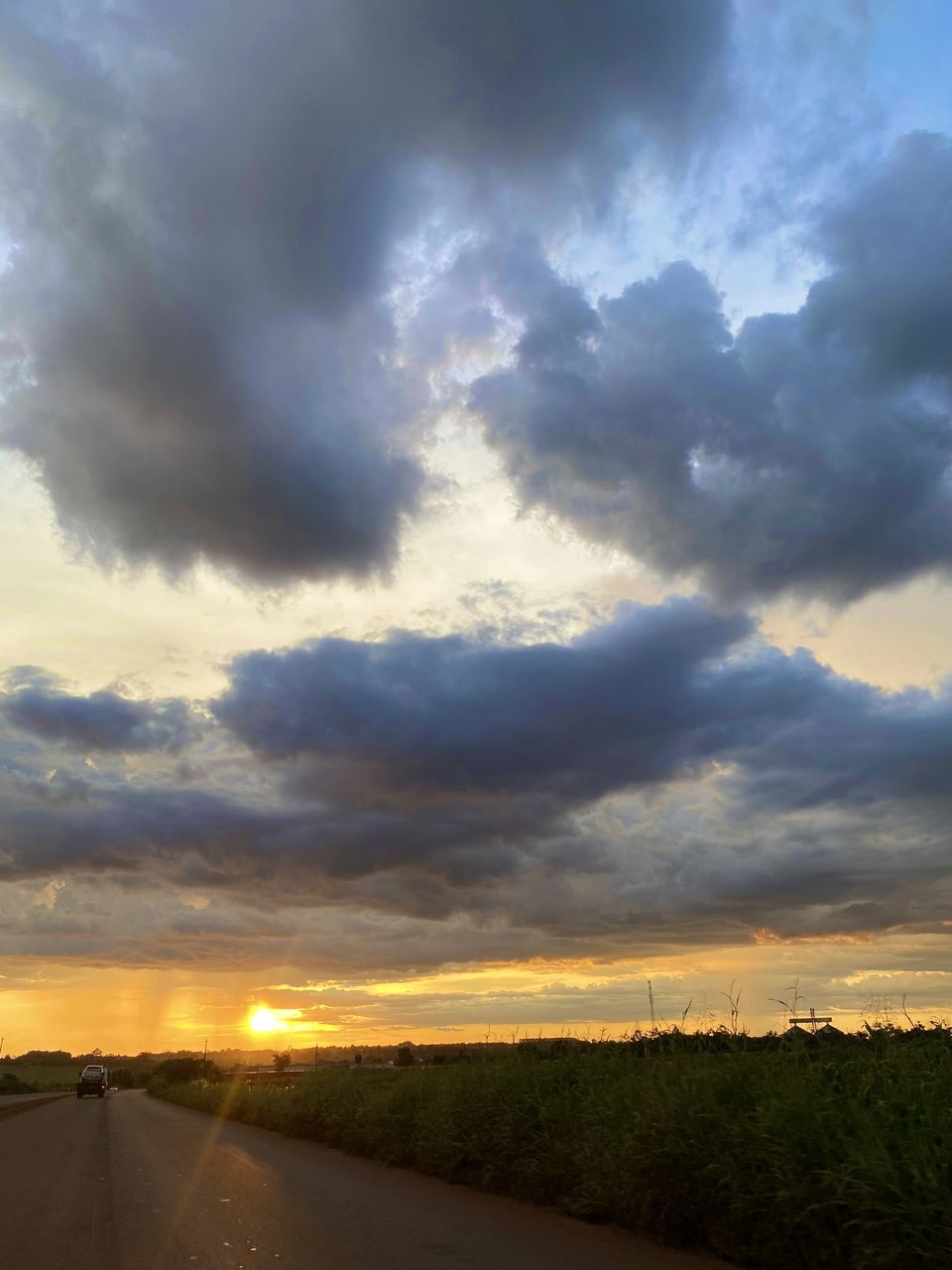 sky, cloud, environment, sunset, road, horizon, nature, landscape, beauty in nature, dramatic sky, transportation, sunlight, scenics - nature, no people, cloudscape, dusk, plant, land, the way forward, evening, rural scene, storm, outdoors, sun, tranquility, field, horizon over land, travel, sunbeam, grass, moody sky, non-urban scene, tranquil scene, vanishing point, street, country road, blue, diminishing perspective