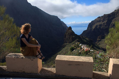 Rear view of woman sitting on retaining wall against mountain