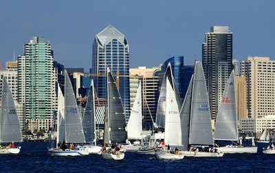 Sailboats in city by buildings against clear sky