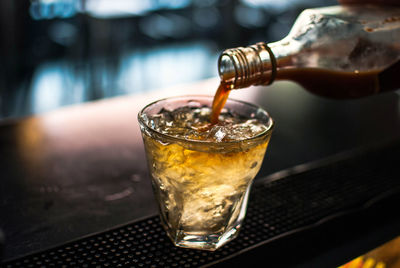 Bottle pouring alcohol in glass with ice cubes on table at restaurant