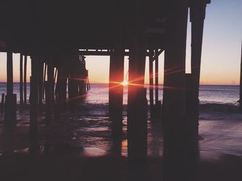 Silhouette pier at beach against sky during sunset