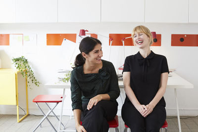 Cheerful mid adult businesswomen sitting on chairs in office
