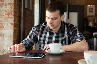 Young man drinking coffee while sitting on table at cafe