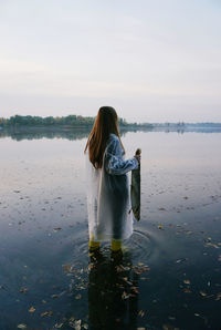 Rear view of woman holding dead fish in lake