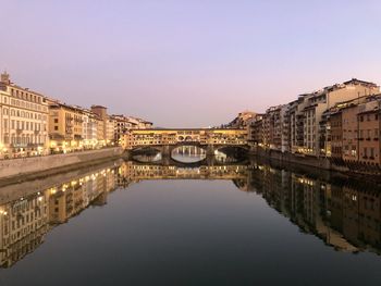 Arch bridge over river by buildings against clear sky