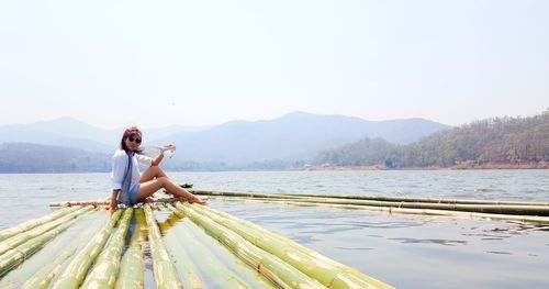 Portrait of woman sitting on raft over lake against clear sky