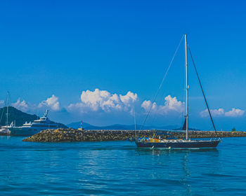 Sailboats moored in sea against blue sky