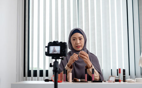 Young woman blogging while applying make up at office