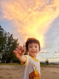 Portrait of smiling boy standing at beach against sky during sunset