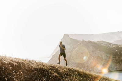 Rear view of man walking on mountain against clear sky