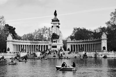 People rowing boat on lake in front of monument building