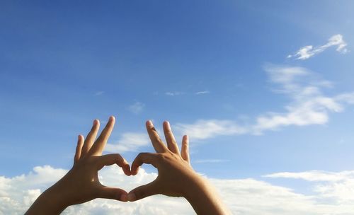 Low angle view of hands holding heart shape against sky