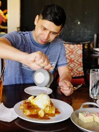 Mid adult man pouring honey in food on plate at restaurant