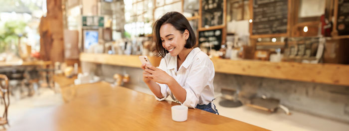 Young woman using mobile phone while standing in cafe