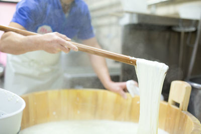 Midsection of worker mixing mozzarella cheese in wooden container at factory