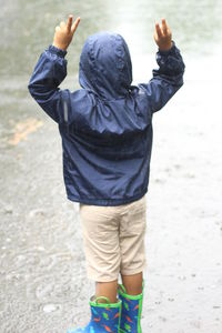 Rear view of boy in raincoat standing on street during rainfall
