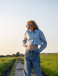 Young woman standing on field against sky