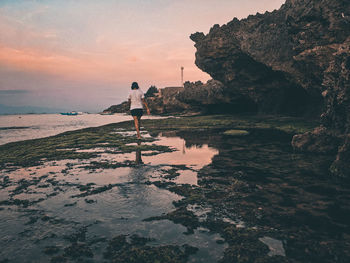 Woman standing on rock at beach against sky