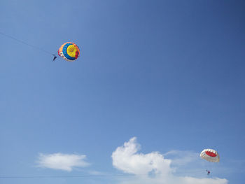 Low angle view of people parasailing against blue sky